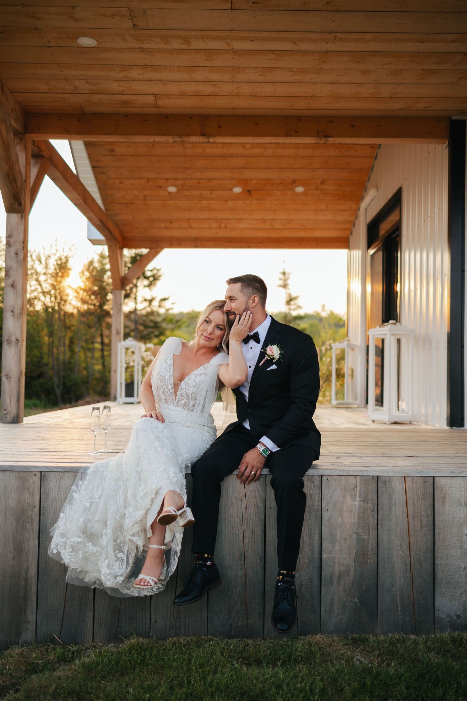 Newlyweds pose playfully along a wooden fence at sunset.