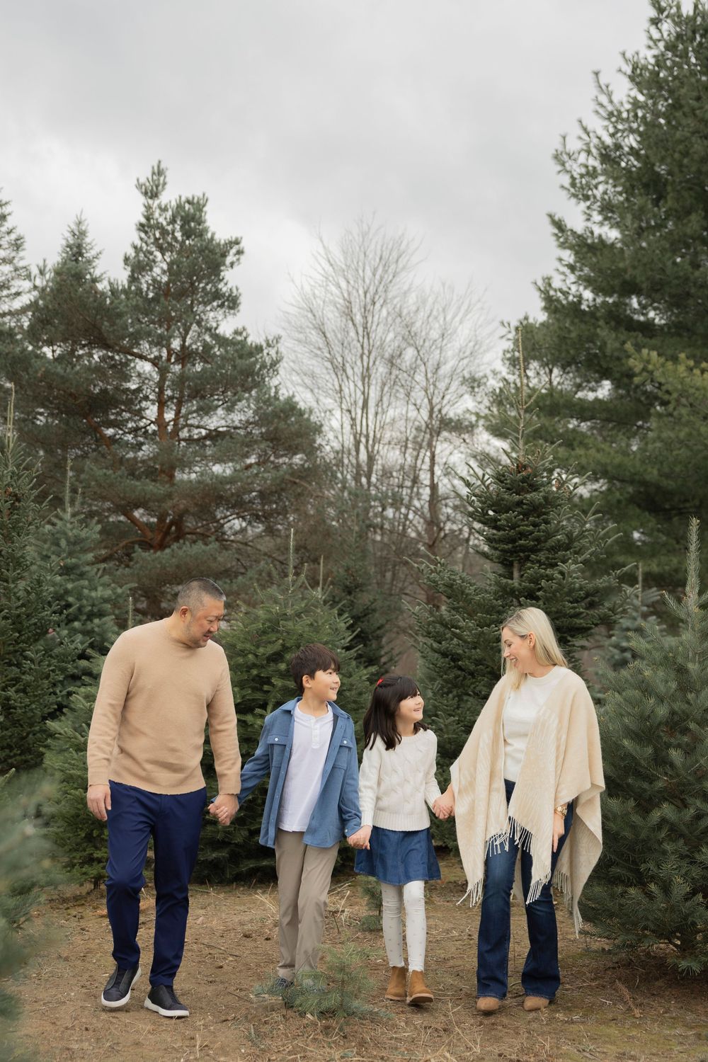 Family wearing coordinated neutral outfits walking together among evergreen trees in an outdoor setting in Rochester hills michigan