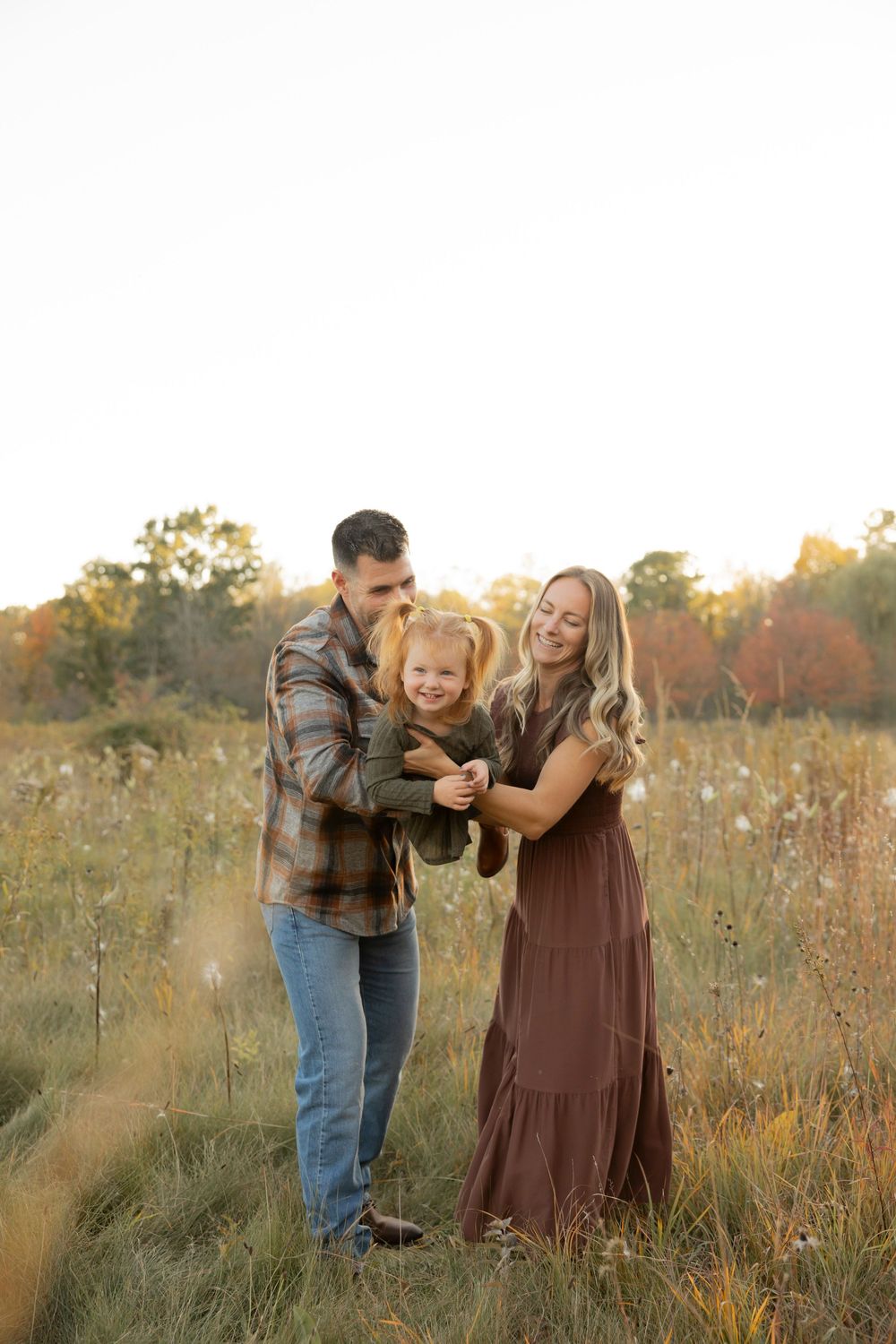 A family playing with their toddler in a golden sunlit meadow during an outdoor photo session at Addison oaks county park in lake Orion