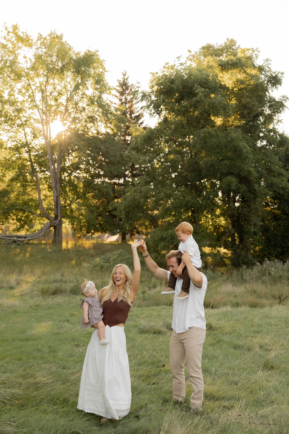 a family with two toddlers dancing in a sunlit field during golden hour at Addison oaks county park in Oakland michigan by lake orion