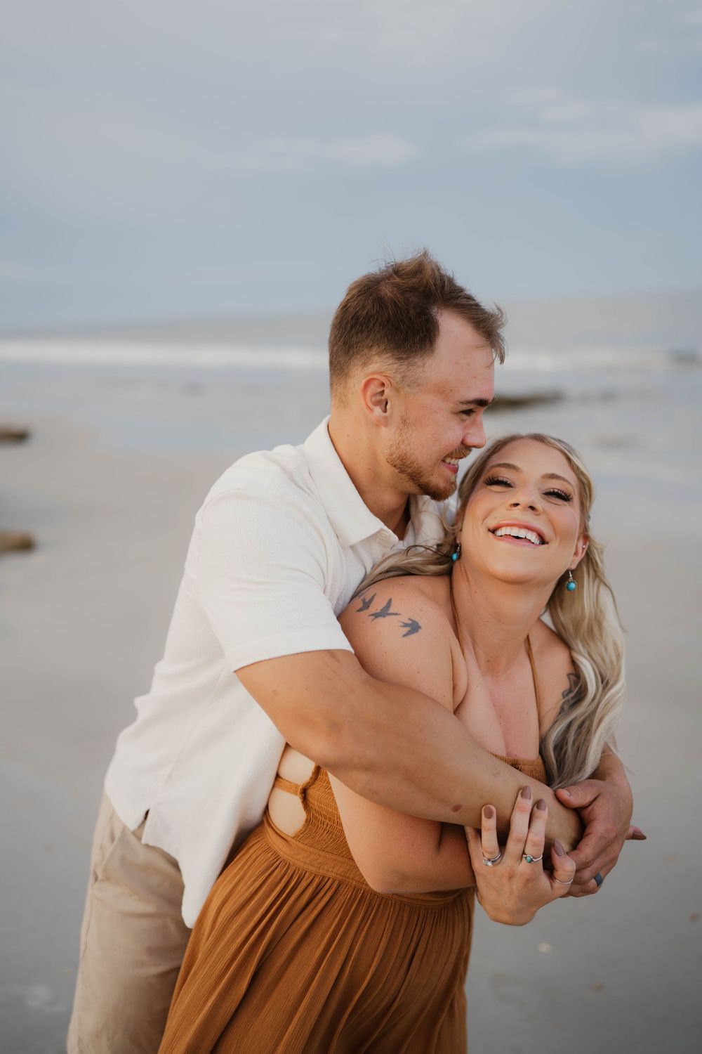 A playful embrace captured on a misty beach with waves in the background.