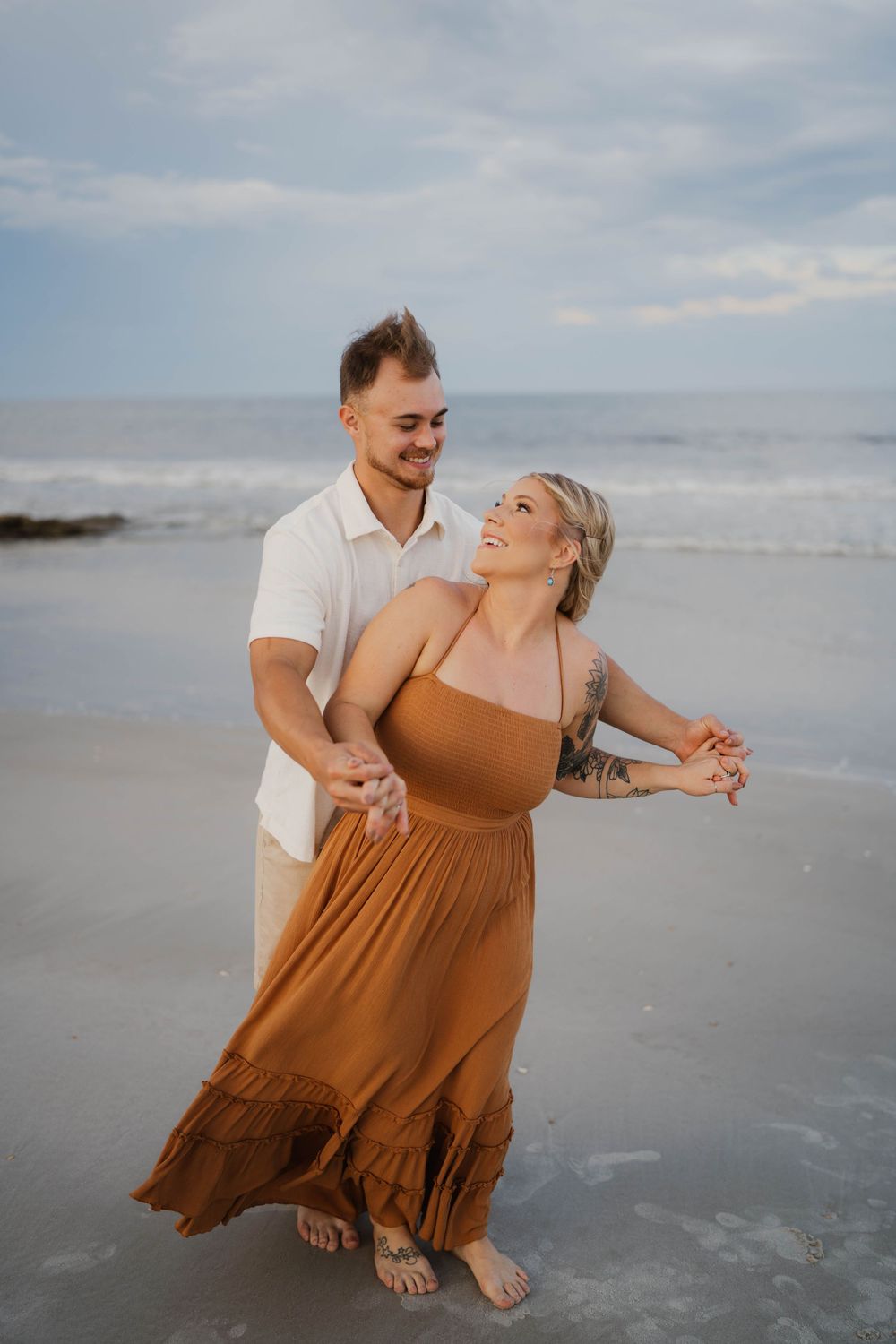 A joyful moment shared between a couple dancing on the beach at sunset.