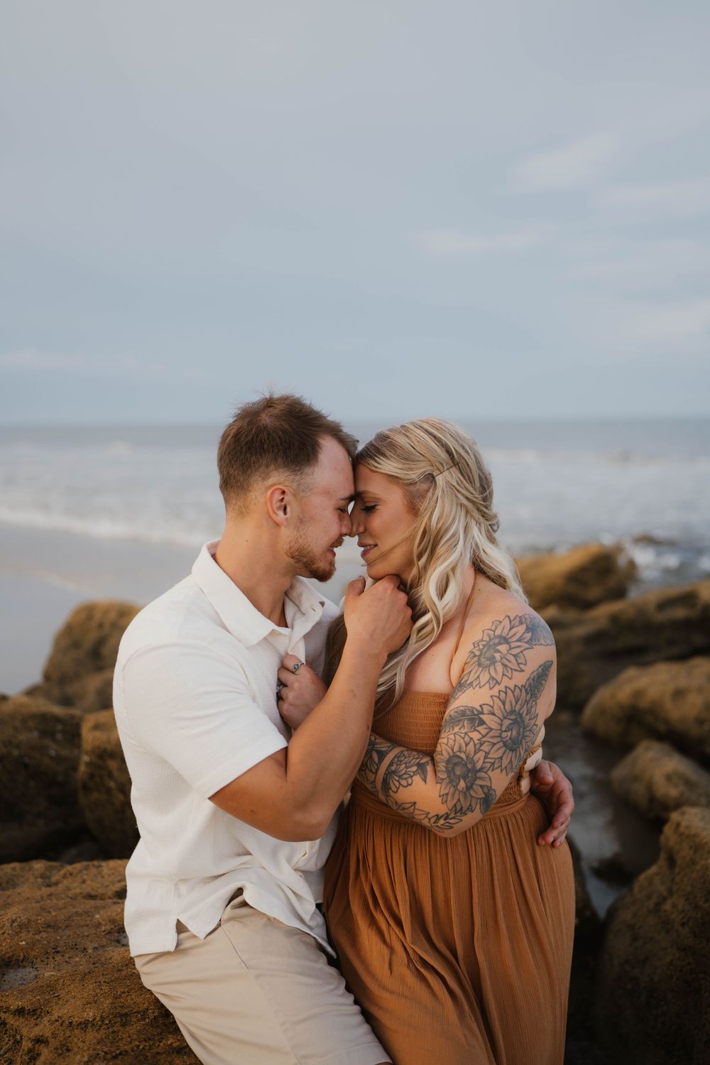 An intimate moment captured between a couple against rocky coastal backdrop.