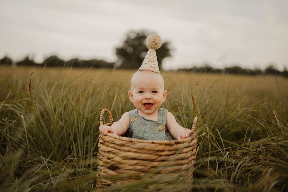 Outdoor portrait of baby sitting in woven basket surrounded by tall grass at sunset.