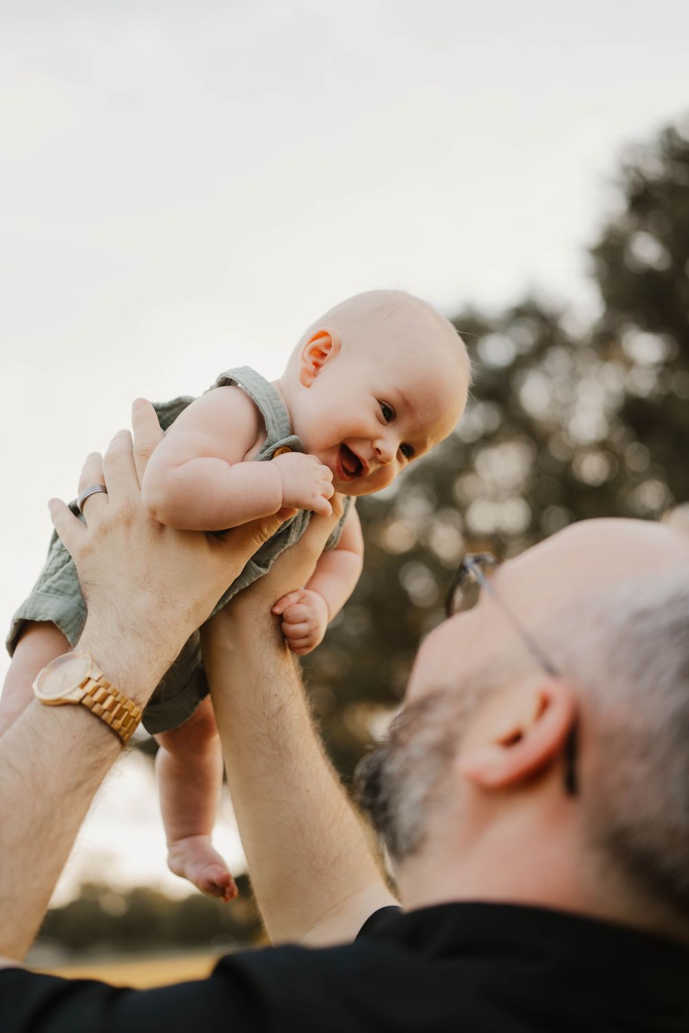 Joyful moment captured during sunset as parent lifts smiling baby into the air.