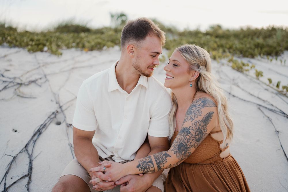 A tender moment shared between a couple sitting in coastal sand dunes.