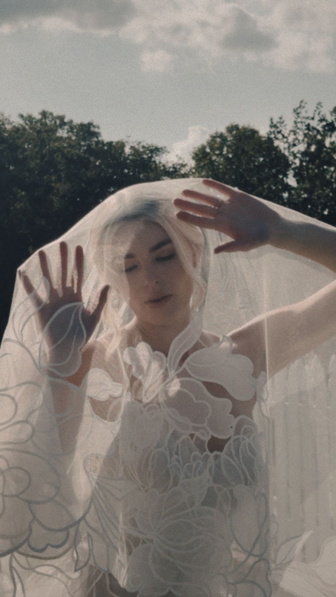 A sequence of ethereal bridal photos showing movement beneath delicate white lace veil against a cloudy sky.