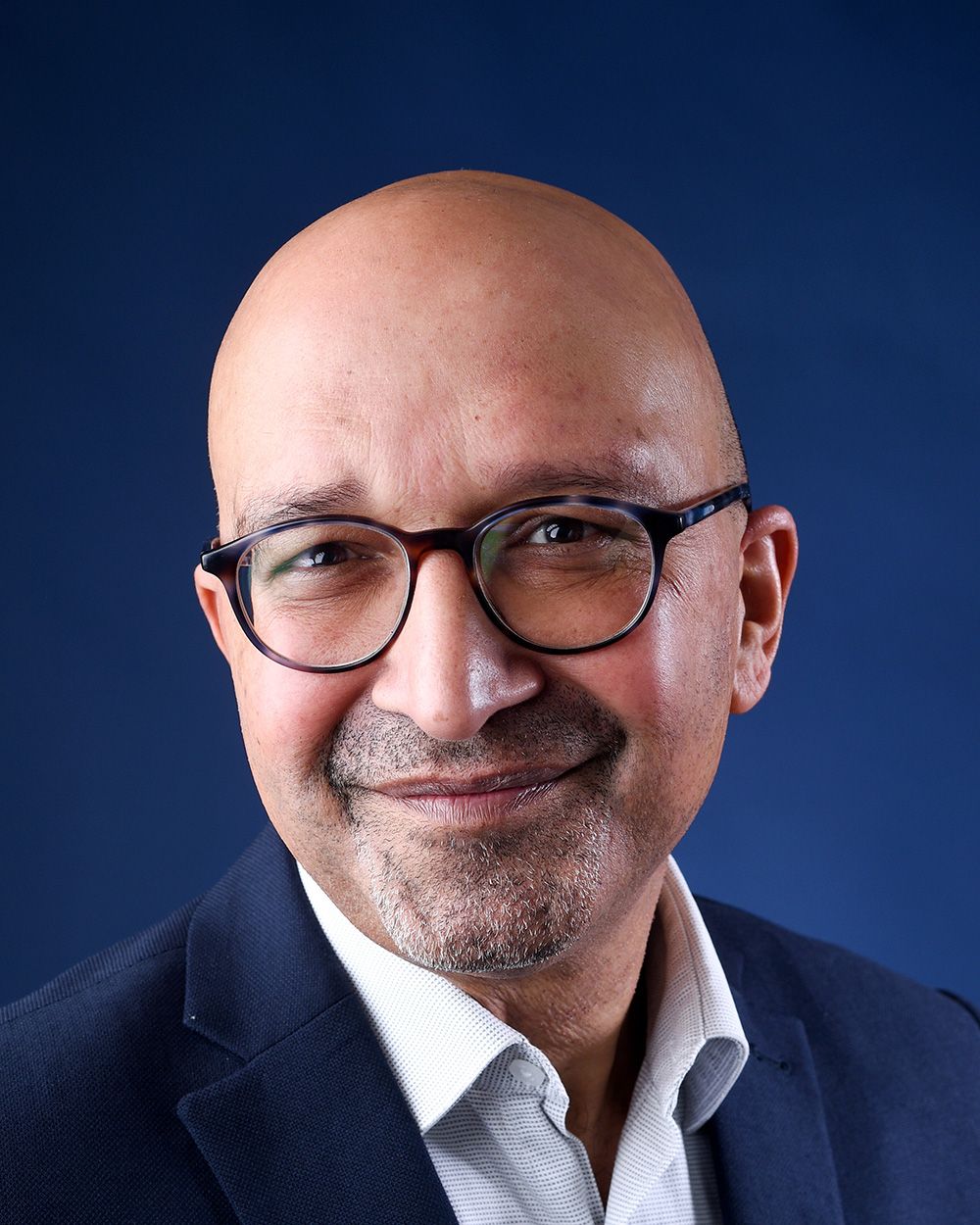 Headshot of a bald man wearing glasses and a suit, set against a dark blue background at Abigail's Studio in Buckinghamshire.