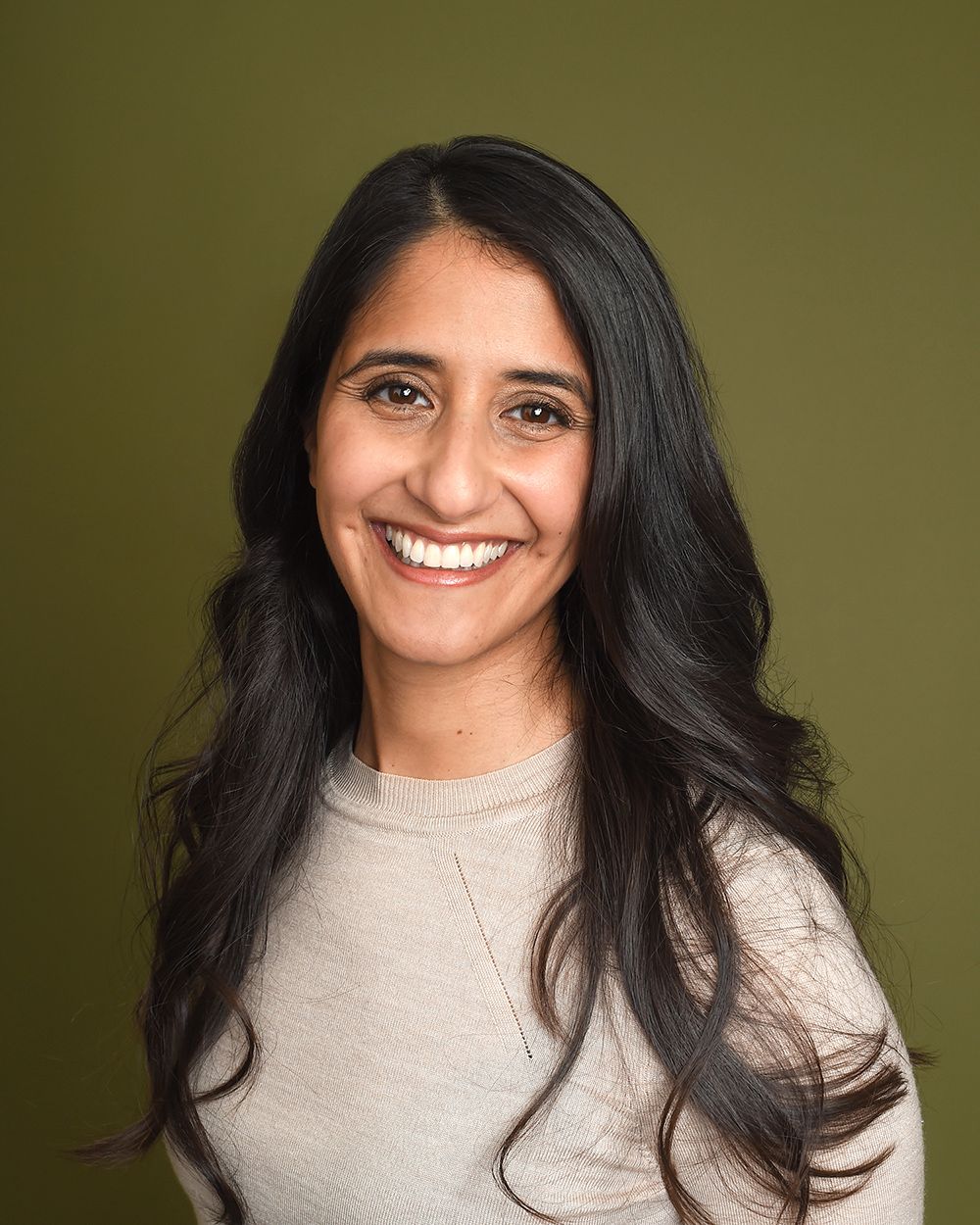 A woman with long hair smiles warmly at the camera against a vibrant green background in a headshot from Abigail's Studio.
