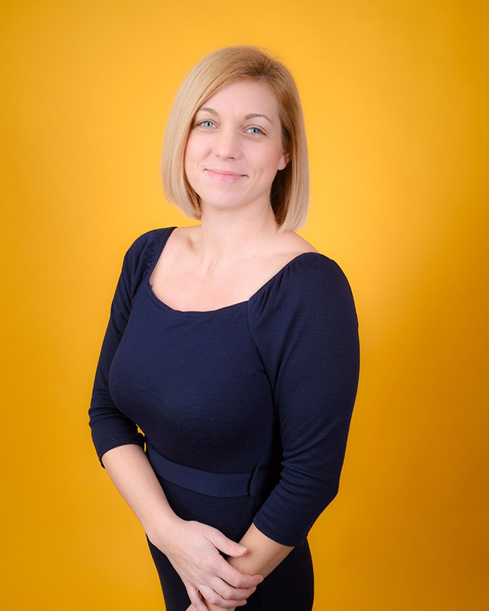 A woman in a black dress poses for a headshot against a vibrant yellow background at Abigail's Studio in Buckinghamshire.