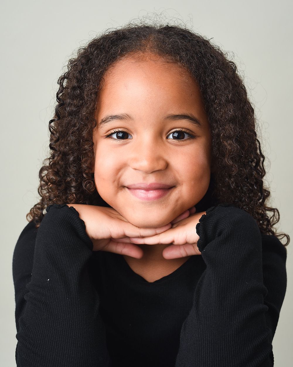 A young girl with curly hair poses for a photo against a light grey background at Abigail's Studio in Buckinghamshire.