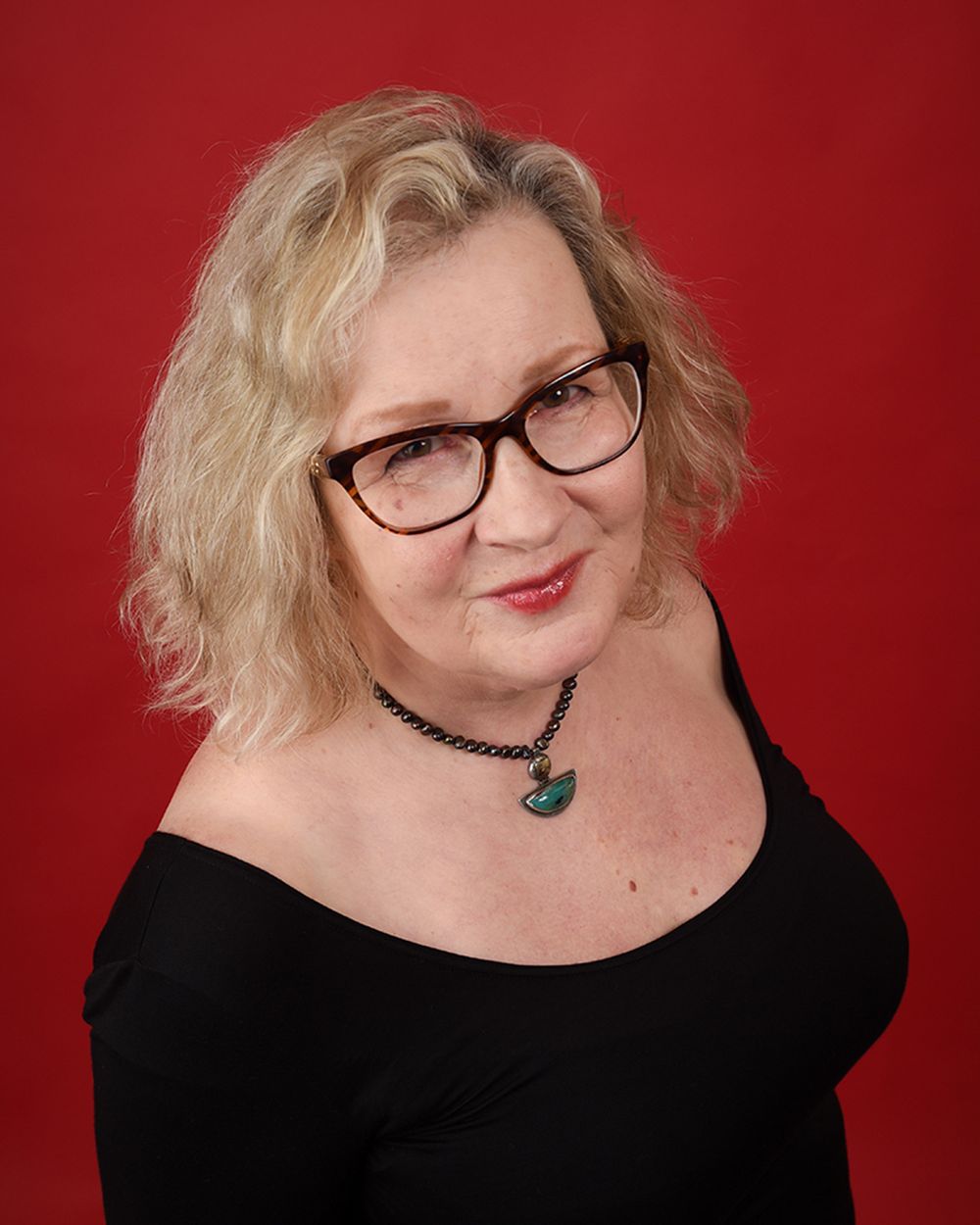 Headshot of a woman in glasses and a black top, set against a striking red background at Abigail's Studio in Buckinghamshire.