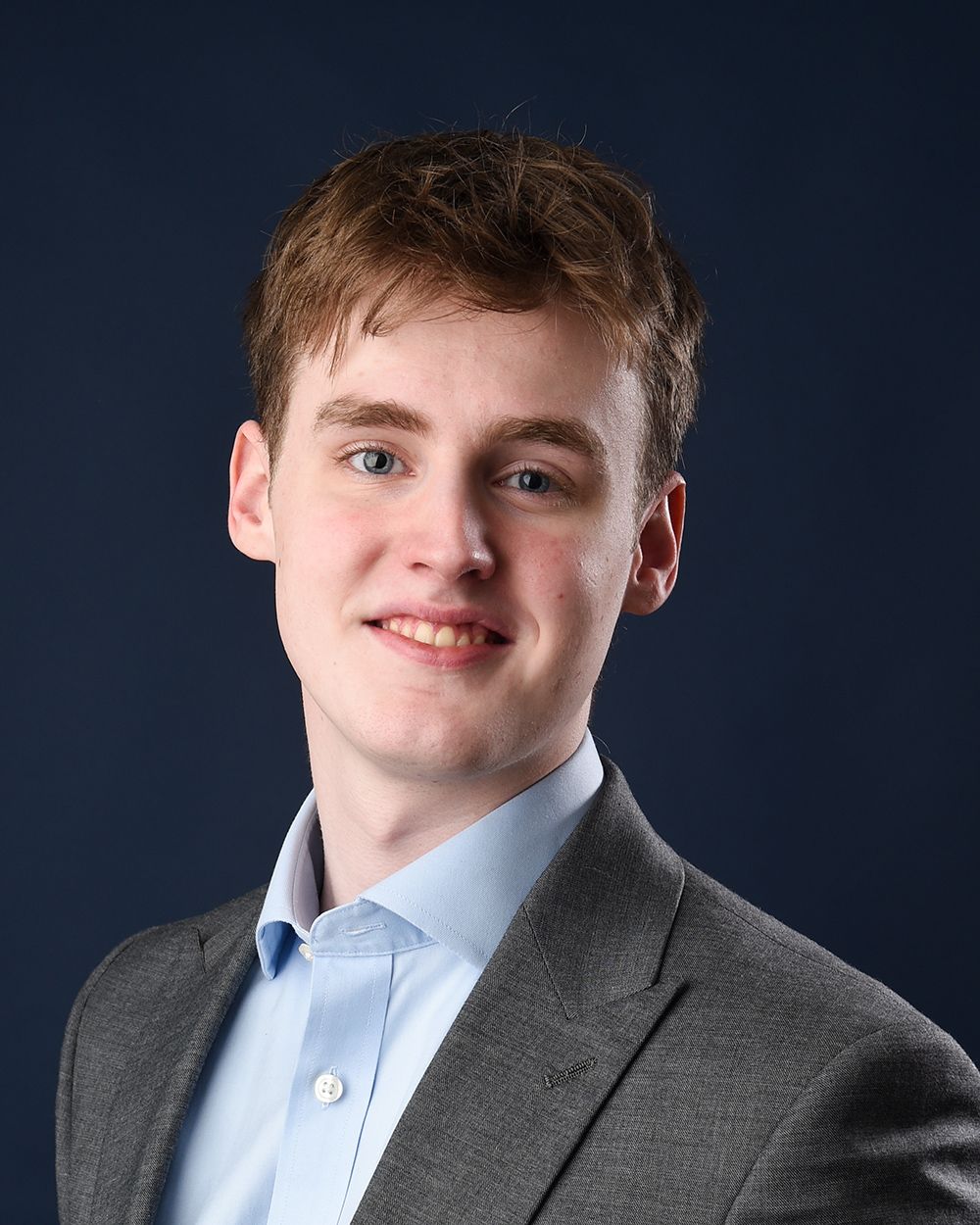 Professional headshot of a young man in a suit and tie, smiling against a dark blue backdrop at Abigail's Studio.