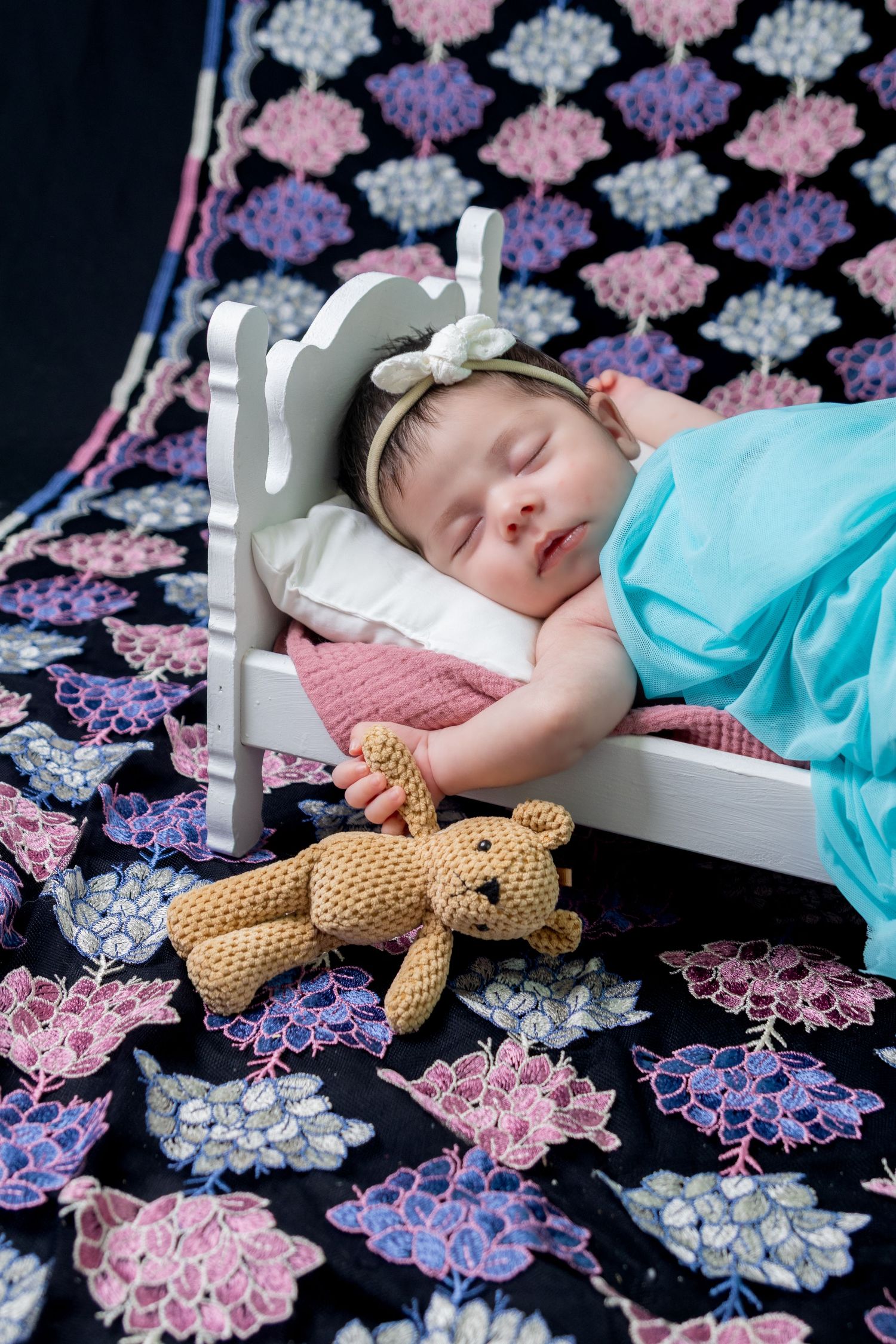 Newborn baby girl peacefully sleeping while holding a small teddy bear during her Seagoville Texas newborn studio photoshoot