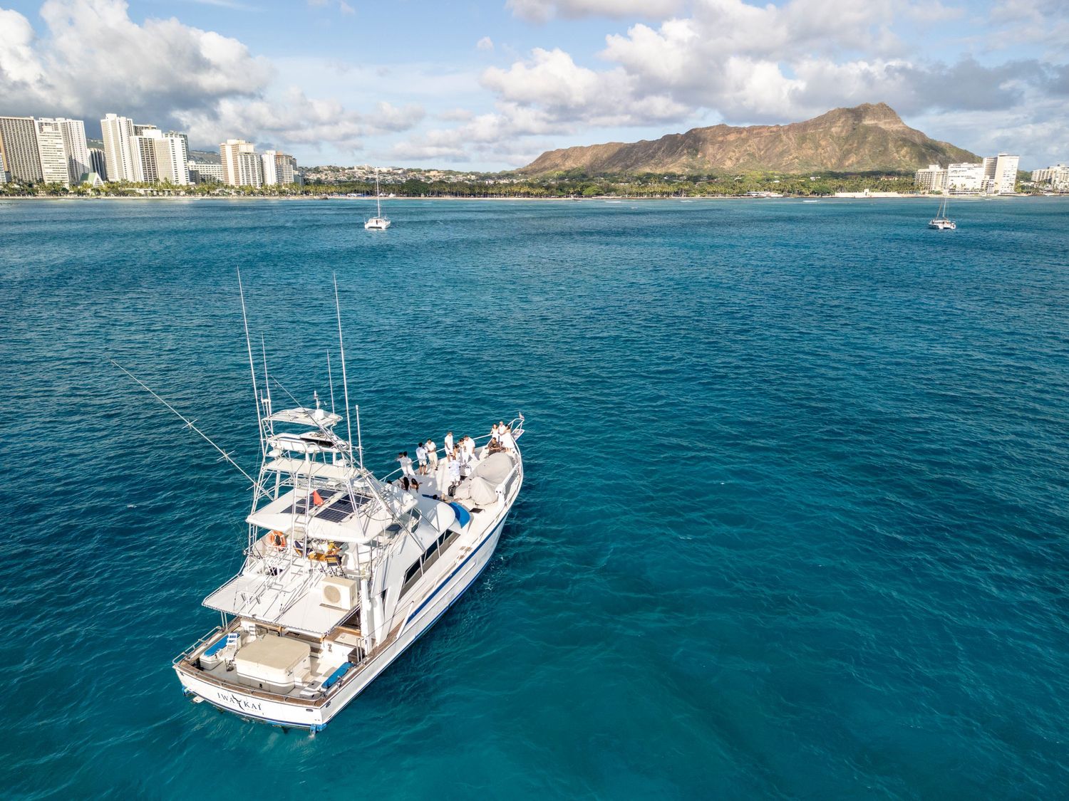 Aerial view of yacht sailing in crystal clear turquoise waters near Hawaiian coastline.