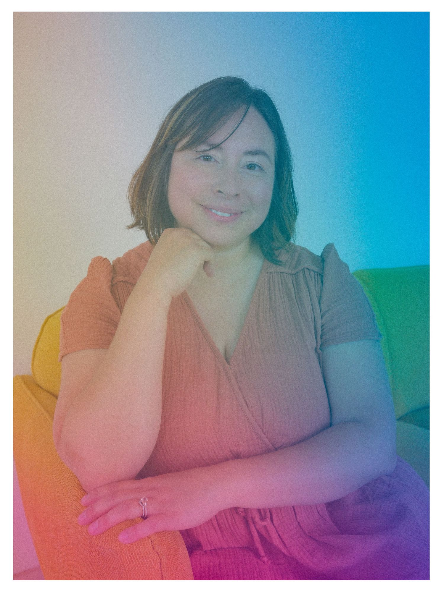 A person wearing an orange top sits relaxed against a rainbow-tinted background with a soft glow effect.