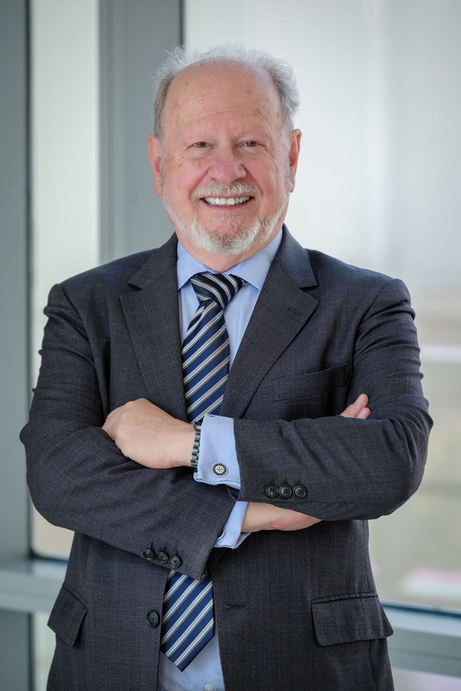 Smiling senior businessman in gray suit and striped tie standing with arms crossed in modern office.