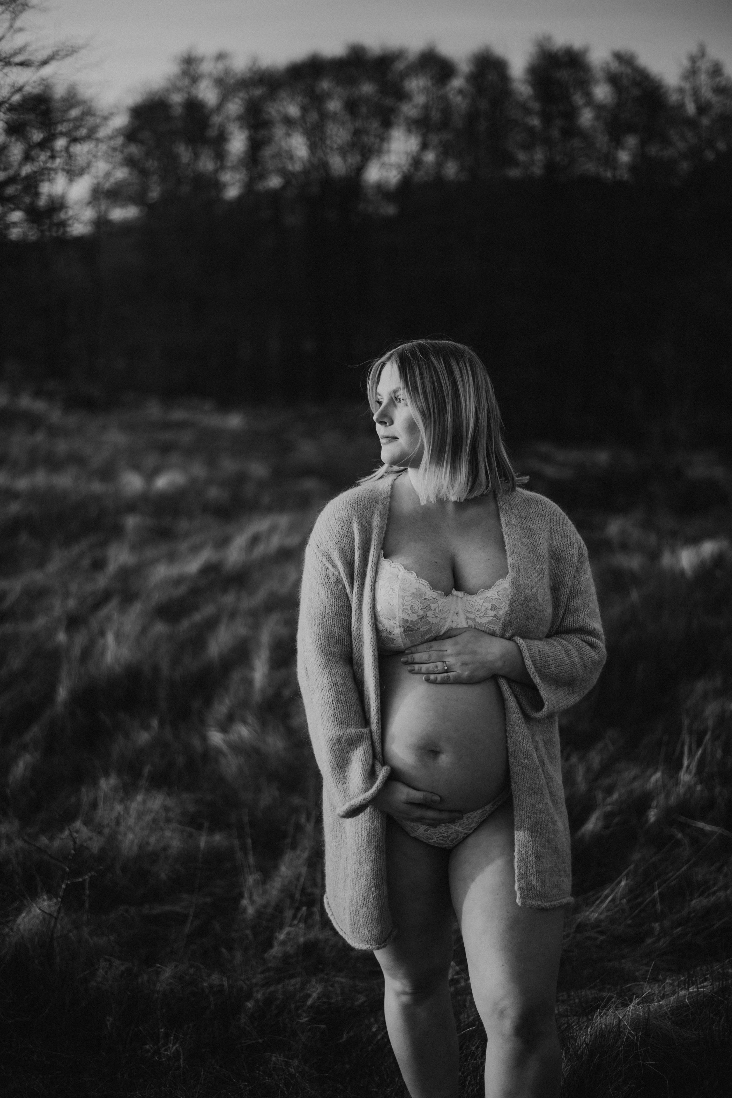 Gravid i stickad kofta på en äng