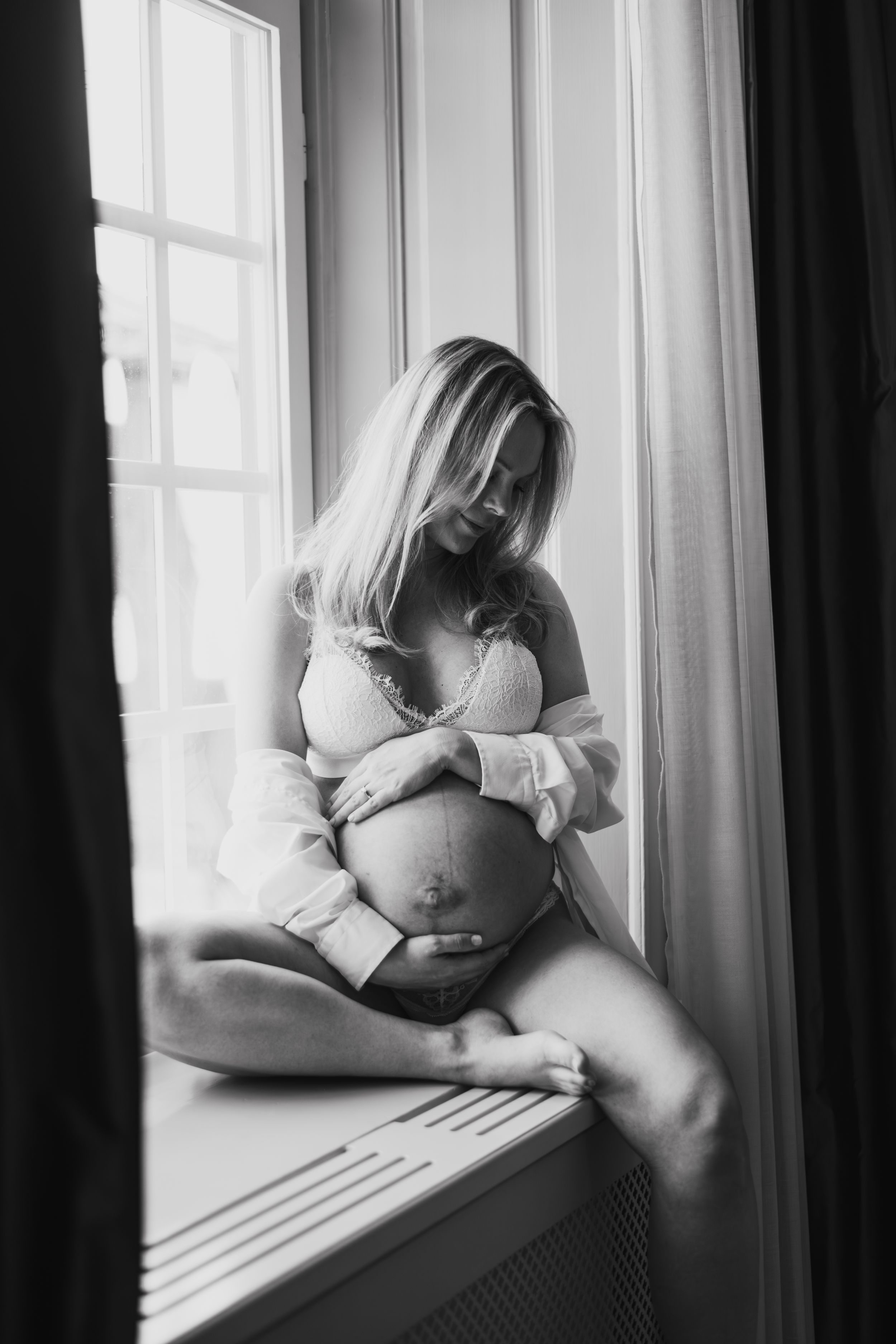 Gravid sitter i fönstret med bar mage