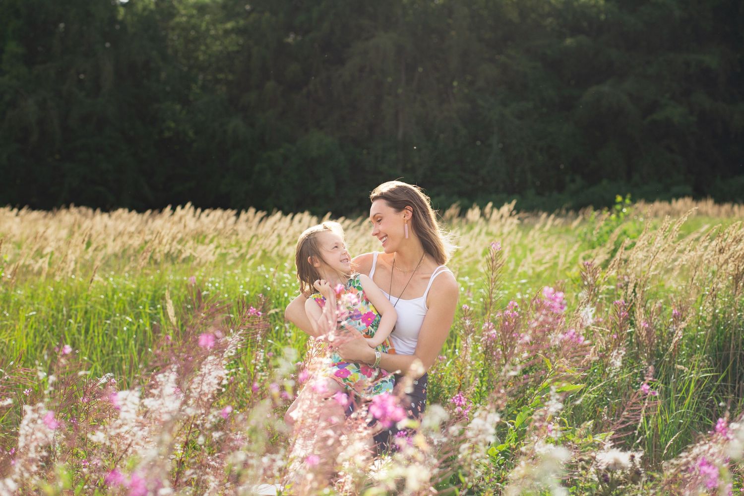 Natural wildflower field with pink blooms and green grass under summer sunlight.