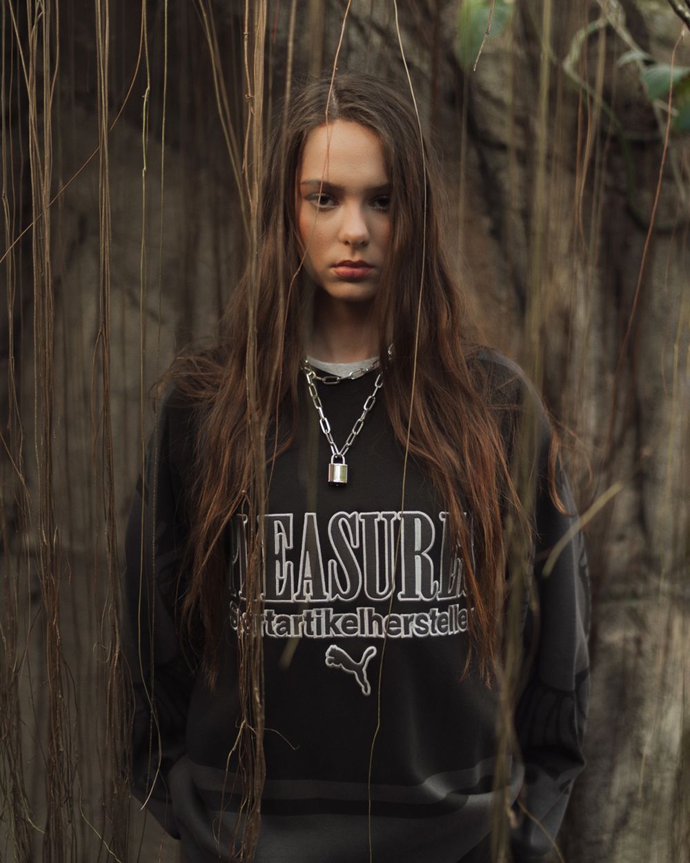 Fashion portrait of a woman with long hair wearing a dark graphic t-shirt, photographed in an atmospheric forest setting