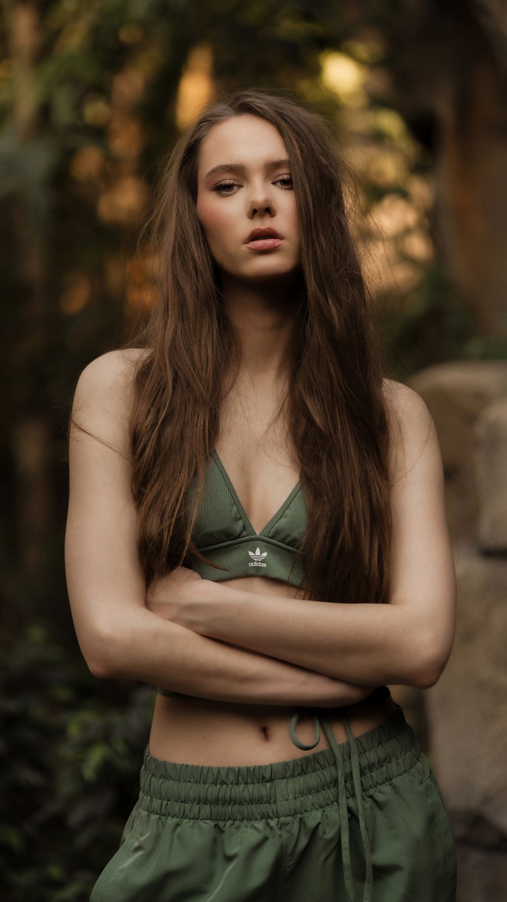 Portrait of a woman in a dark green top with arms crossed, photographed in a lush tropical outdoor setting