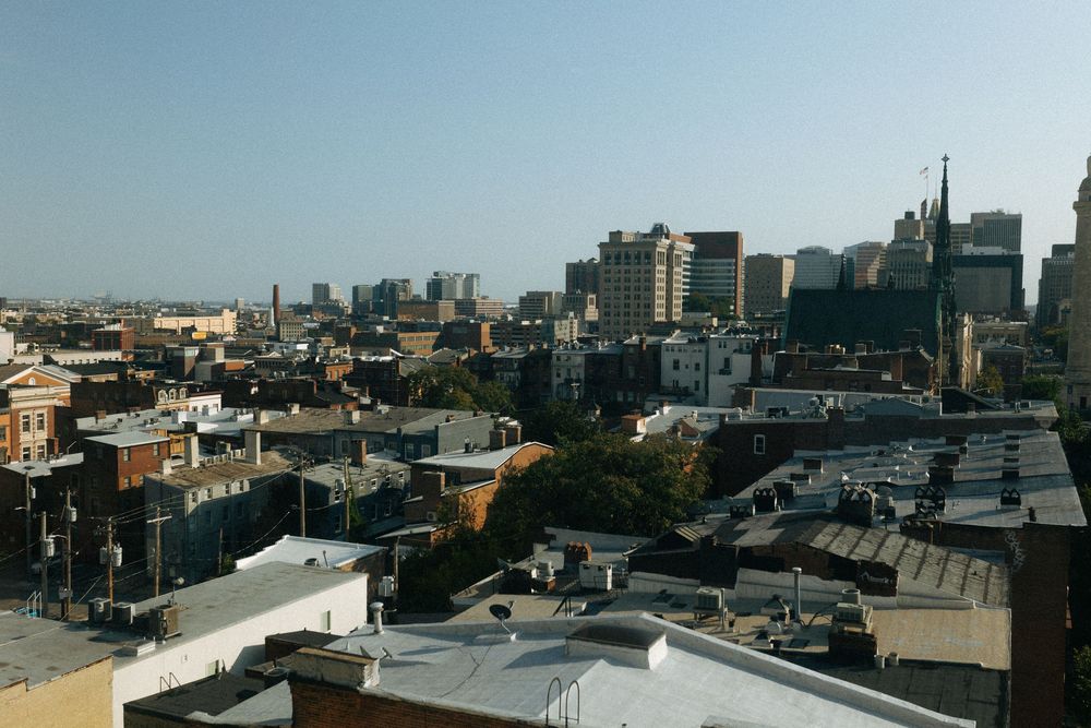 Panoramic cityscape view showing urban rooftops and buildings against a bright daytime sky.