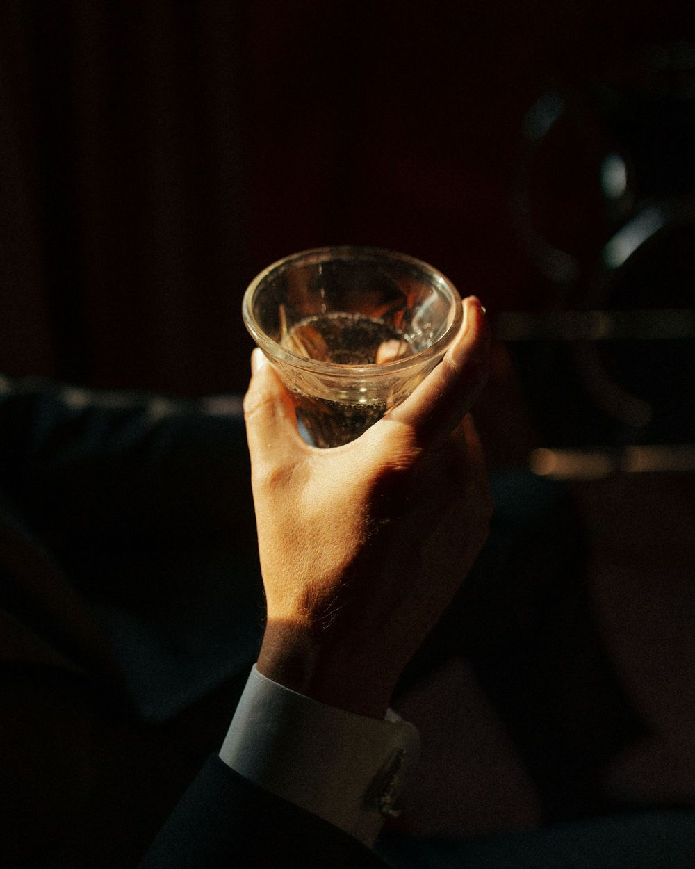 A hand holding up a glass of champagne or white wine in a dimly lit setting.