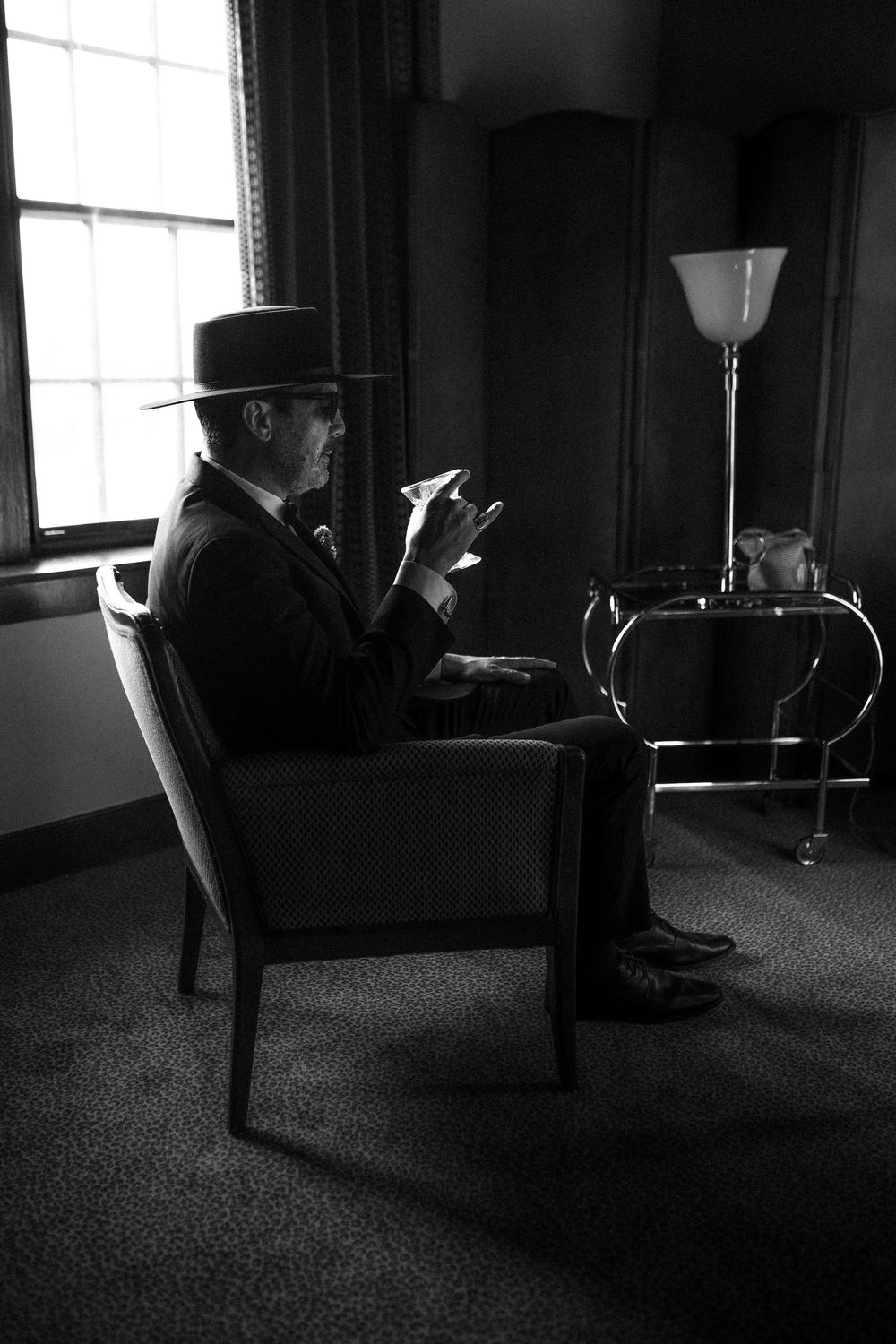 A silhouetted figure sits in an armchair smoking in a dark room with a floor lamp.