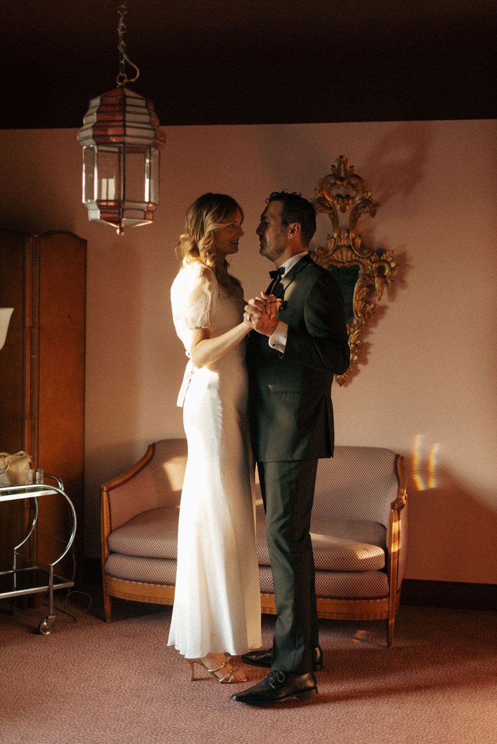 Romantic couple dancing in dimly lit room with ornate lantern and vintage decor.