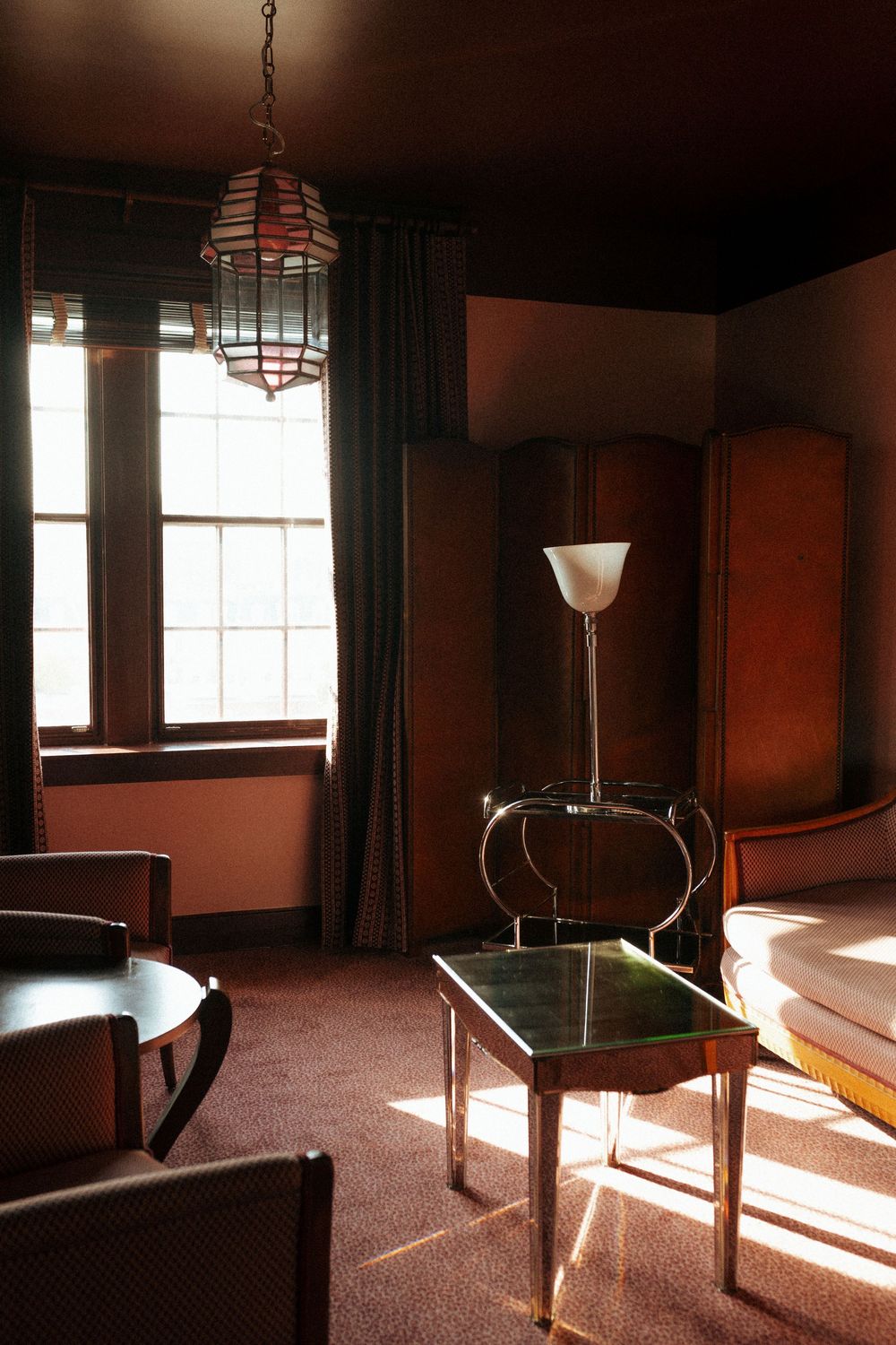 Sunlit empty room interior with vintage floor lamps casting dramatic shadows across carpeted floor.