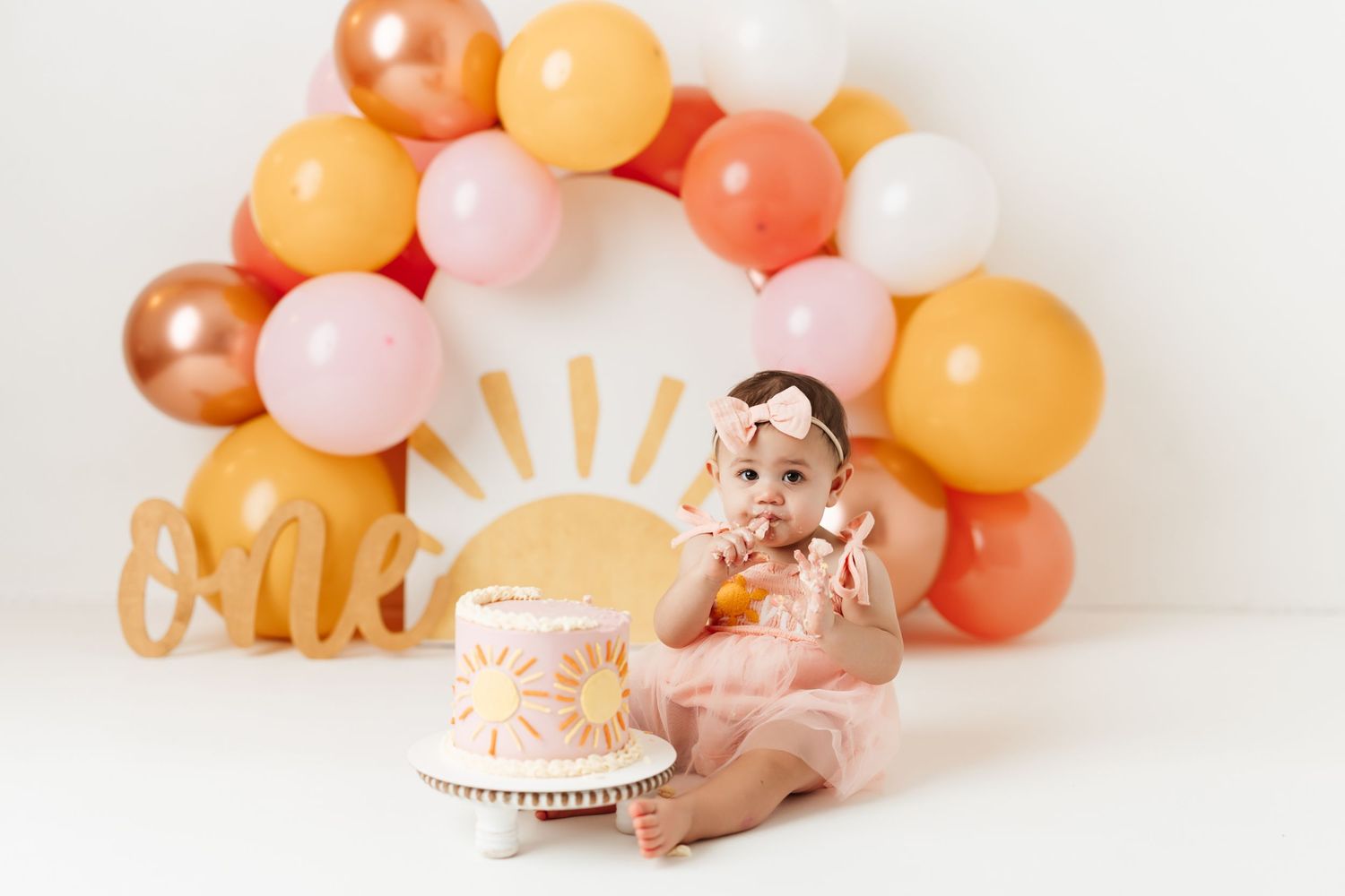 One-year cake smash session with pastel balloon arch and sunshine-themed birthday setup at Anna Carreno Photography in Magnolia, Texas.