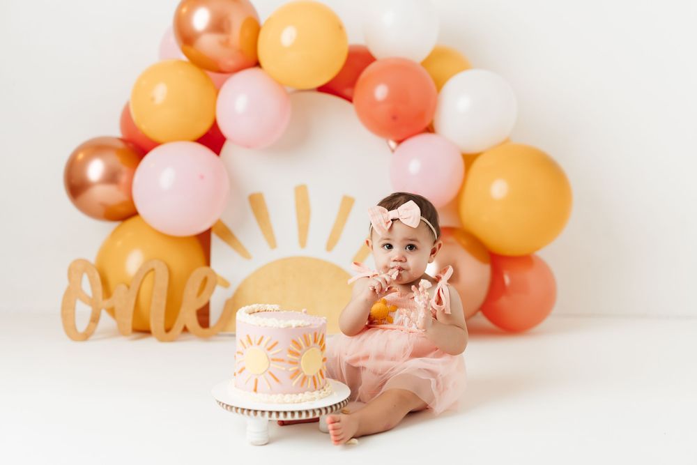 One-year cake smash session with pastel balloon arch and sunshine-themed birthday setup at Anna Carreno Photography in Magnolia, Texas.