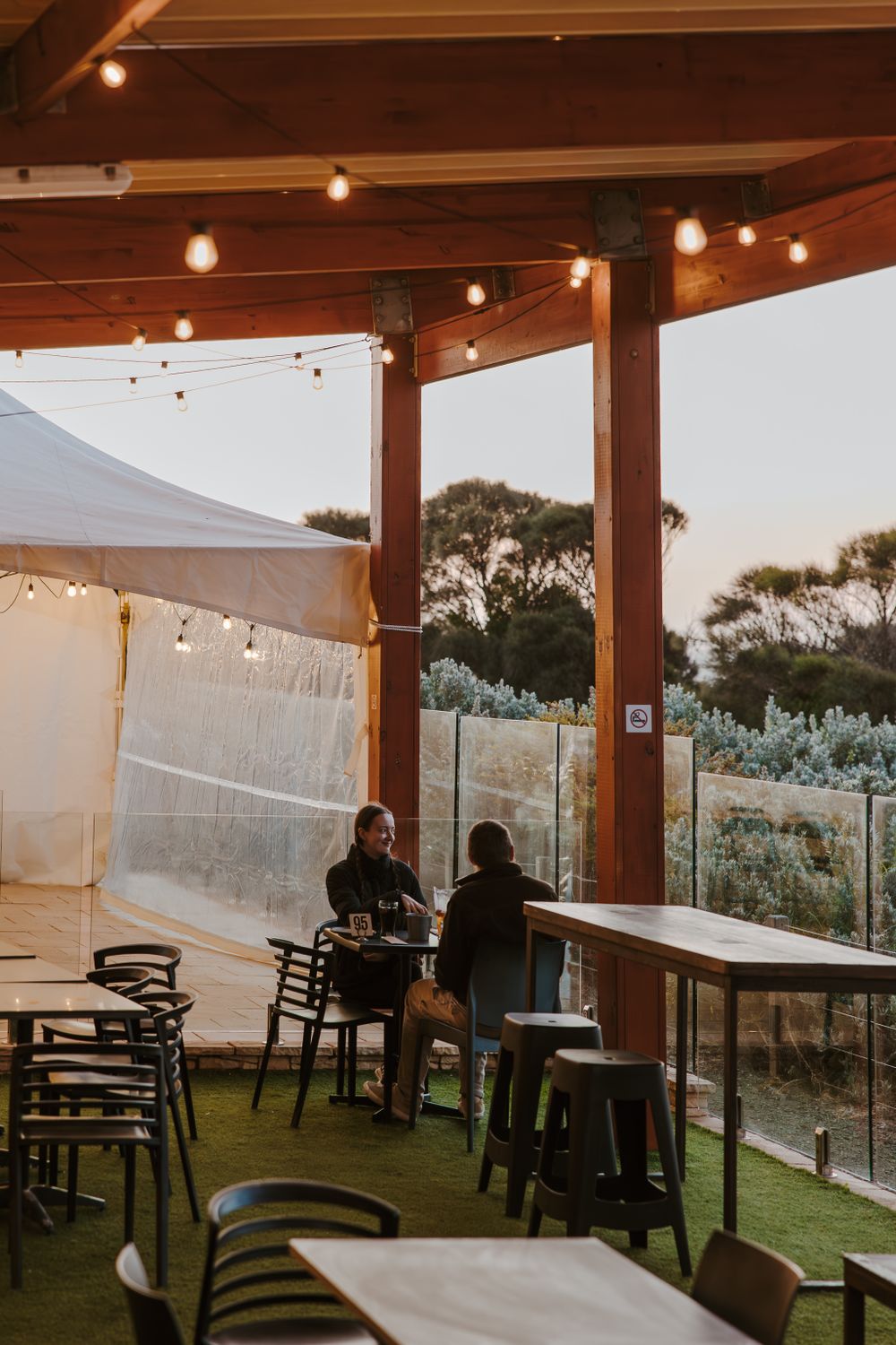 Outdoor dining area with string lights and tables under a covered patio at dusk.