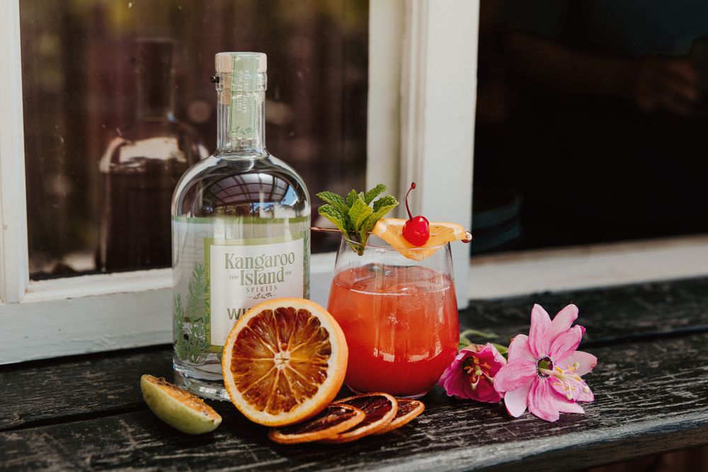 Tropical cocktail with blood orange garnish and pink flowers served on a rustic wooden surface.