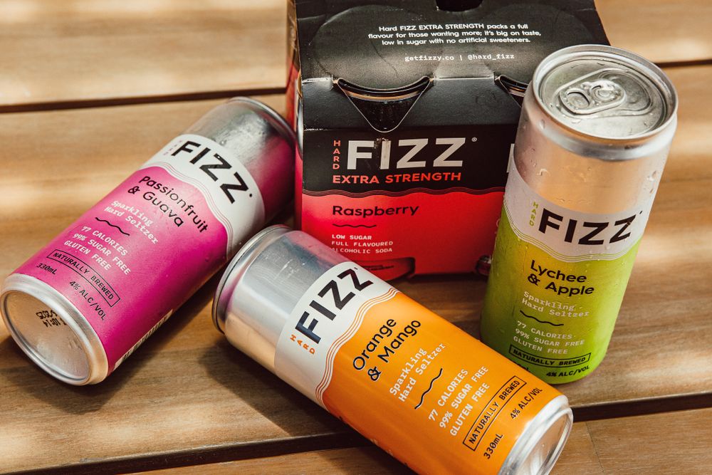 Various flavors of FIZZ canned drinks displayed on wooden table with promotional materials.