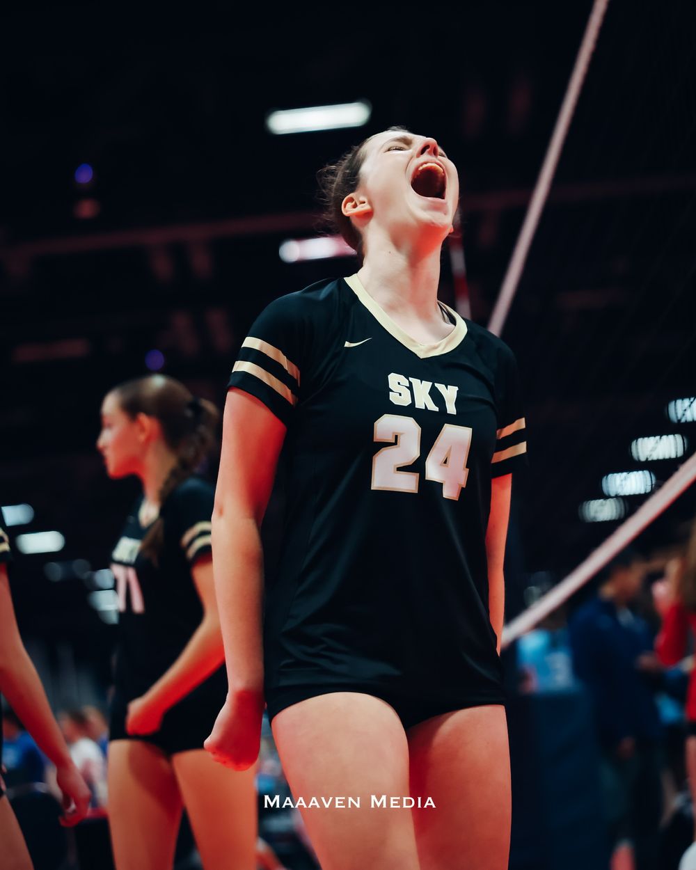 Volleyball player #24 in black SKY jersey celebrates with mouth open during an intense match.