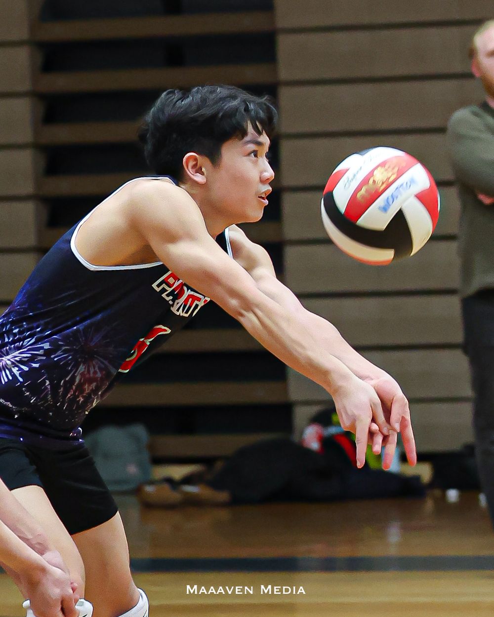 Young male volleyball player in navy uniform performing a dig during an indoor match.