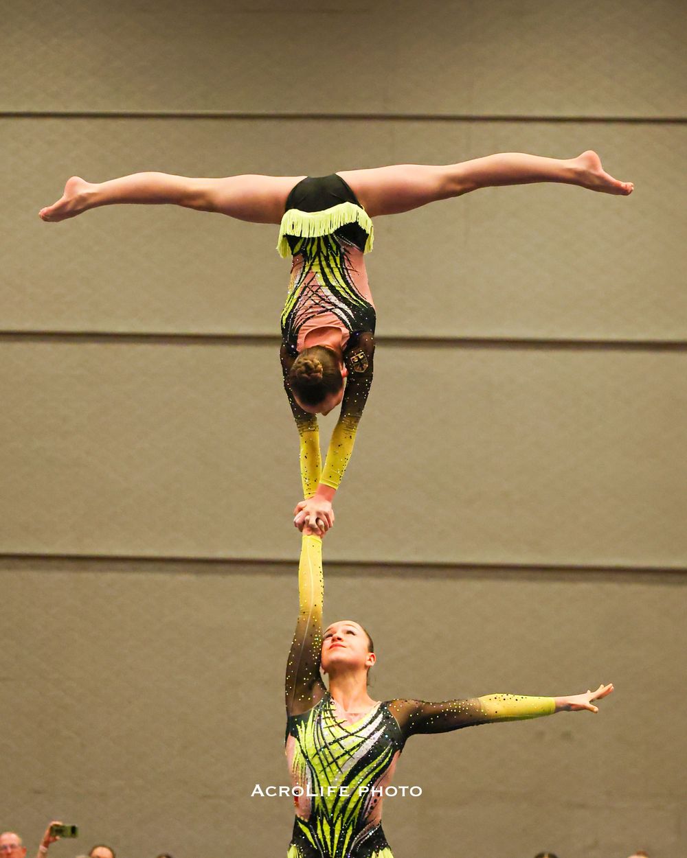Two acrobatic gymnasts perform a stunning balance act, with one athlete held horizontally aloft by their partner below.