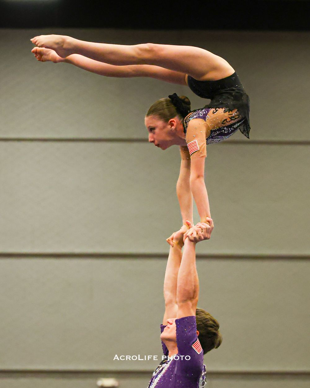 Two female acrobatic gymnasts performing a hand-to-hand balance skill during competition.