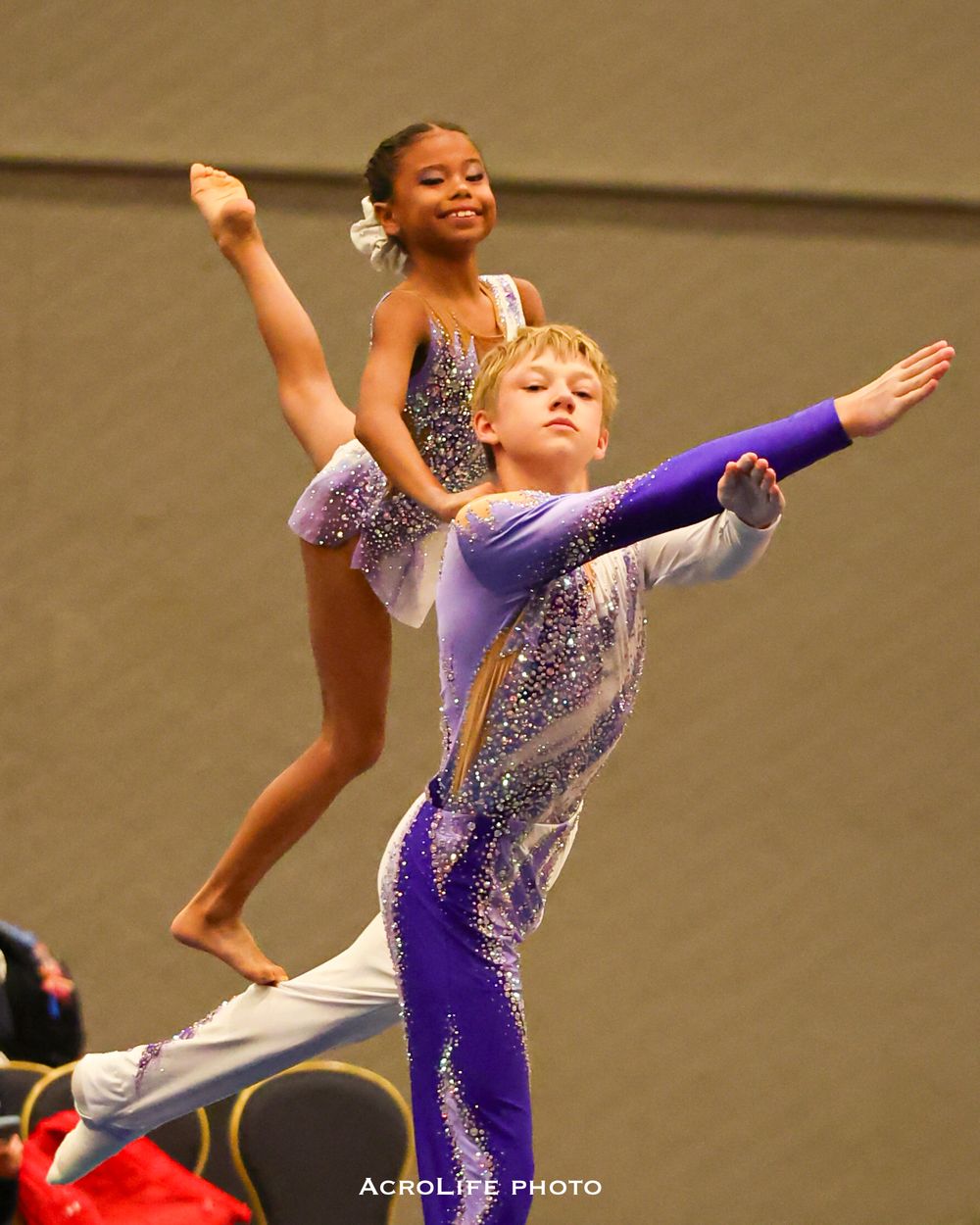 Young boy and girl performing acrobatic gymnastics pair routine in sparkly competition leotards.