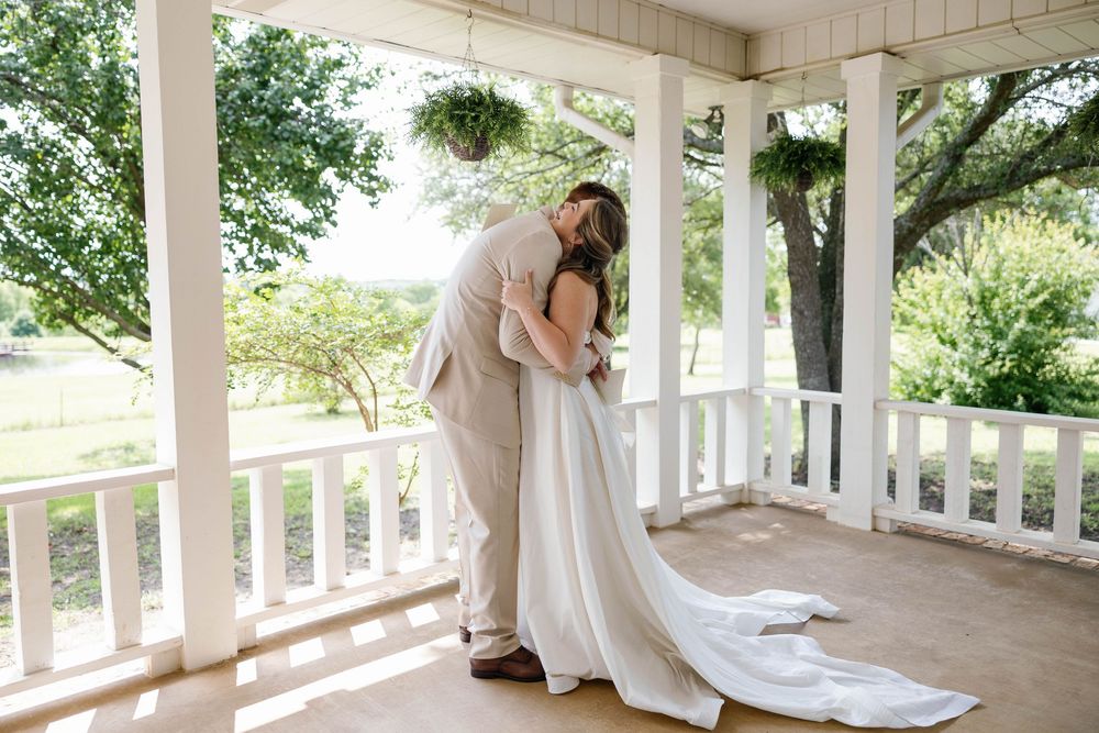 Bride and groom sharing intimate first look embrace on a white porch with garden views.