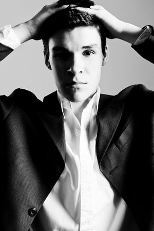 Black and white portrait of a young man in a suit with hands on his head.