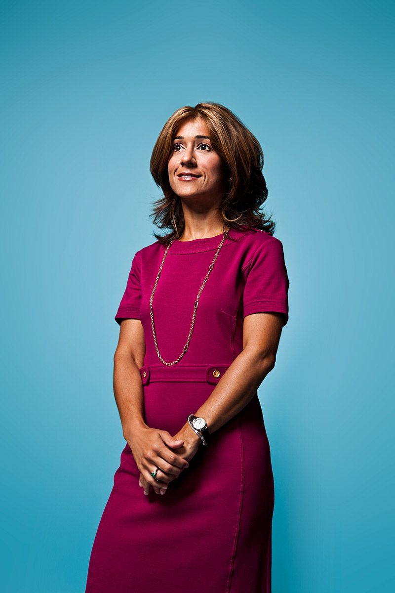 Woman in magenta dress with gold necklace poses against bright blue background for professional portrait.