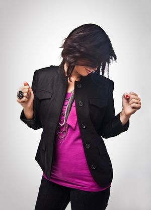 A woman in a black blazer and pink top dances energetically with her hair flying.