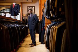 A well-dressed Black man browses suits in an upscale clothing store.