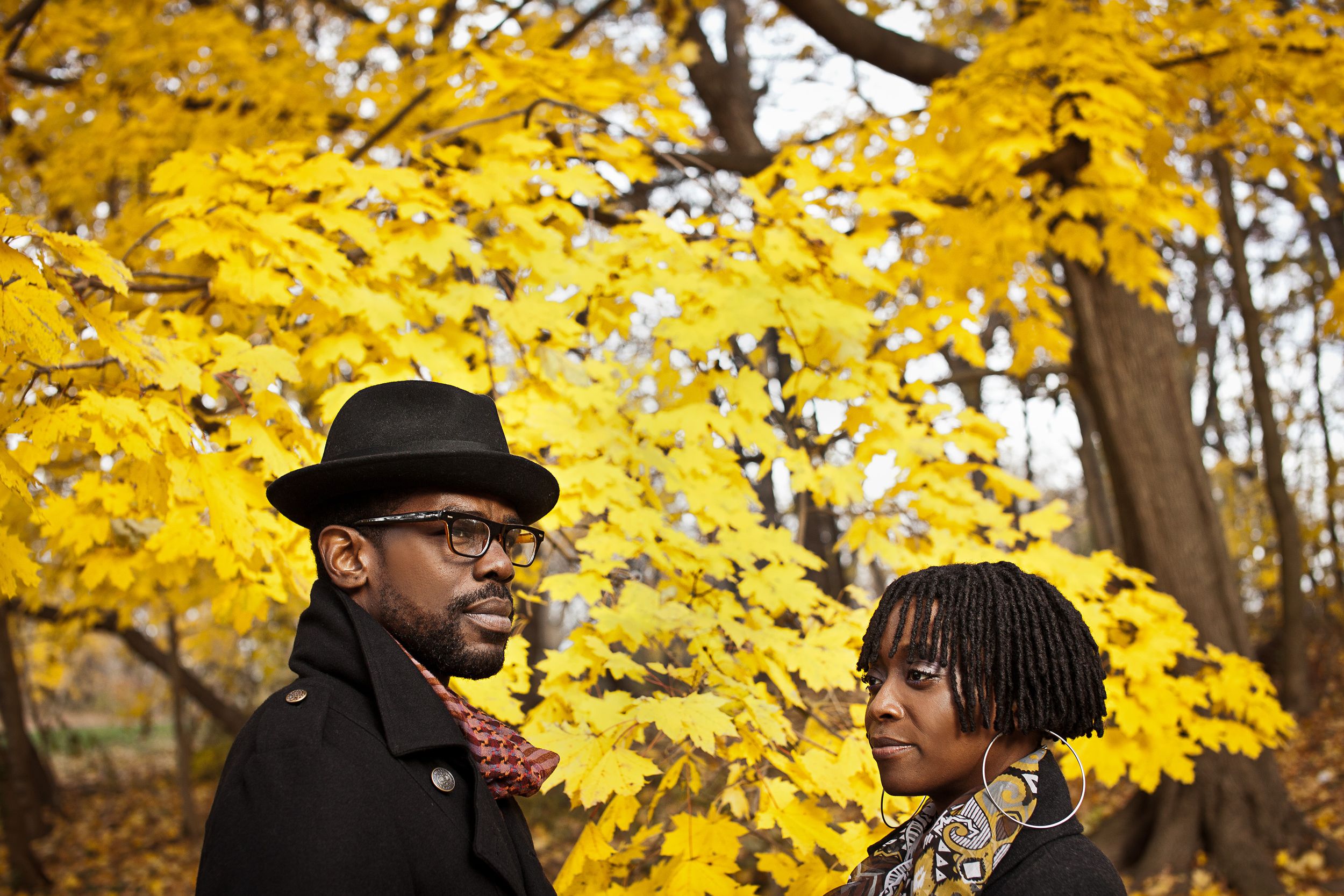 Black couple posing together among vibrant yellow autumn foliage in a park.