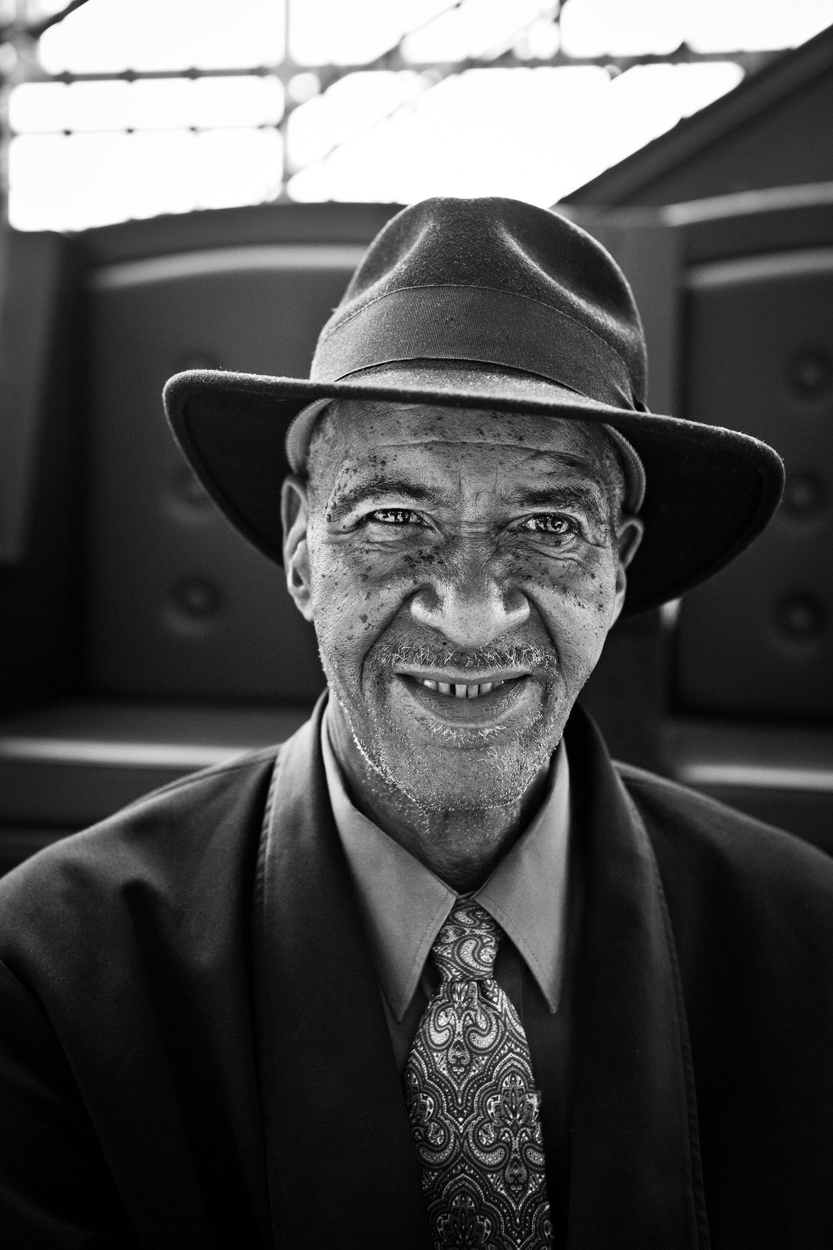 Black and white portrait of a smiling elderly man wearing a fedora hat and tie.