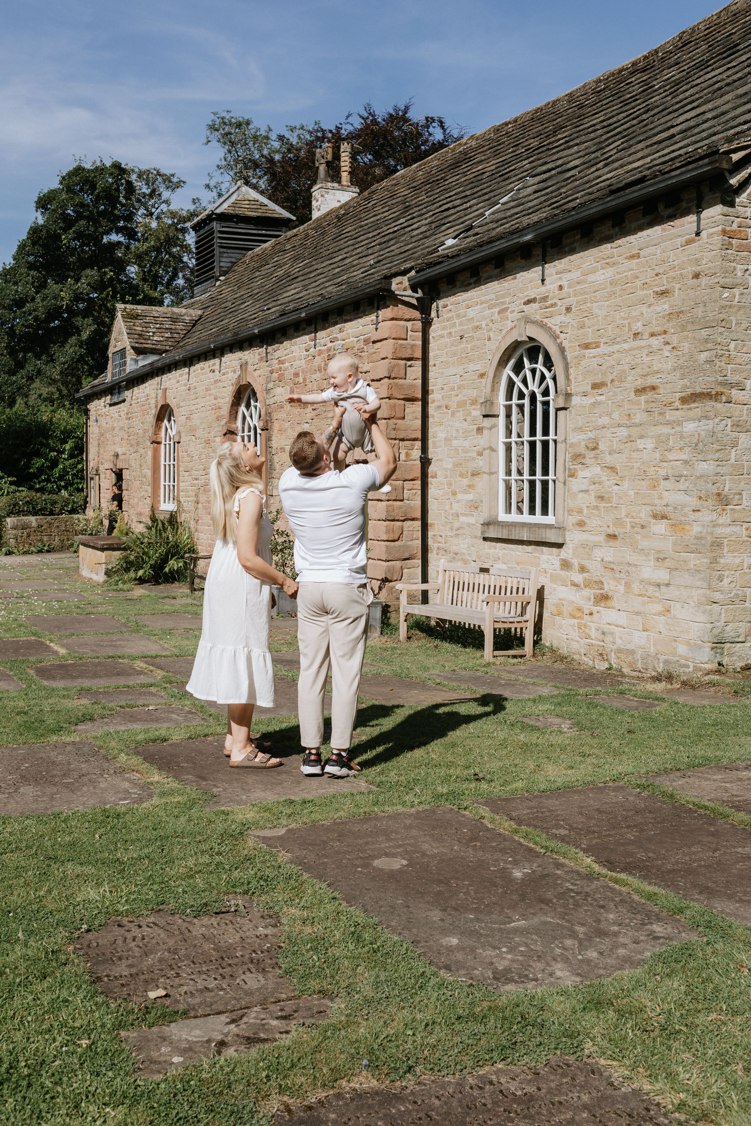 A couple stands facing a stone church building with arched windows on a sunny day.