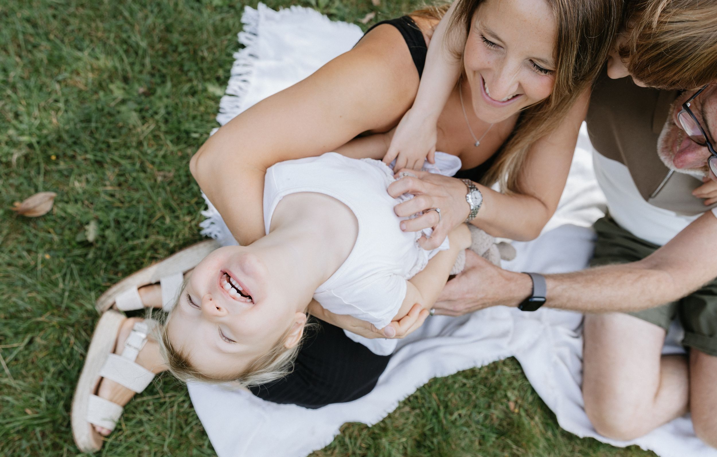 A joyful moment shared on a blanket in the grass during a sunny day outdoors.